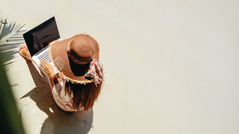 Woman sitting in the sand working on a laptop